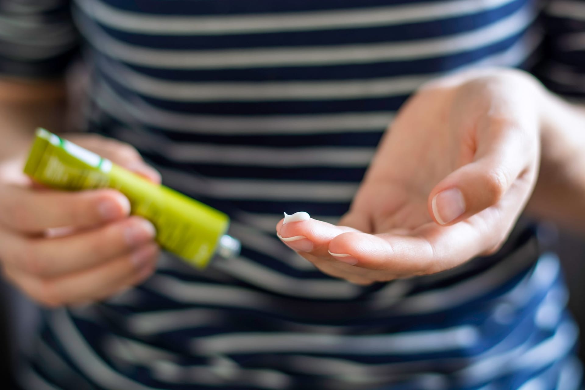 Frau mit Cremetube und etwas Creme auf dem Finger.