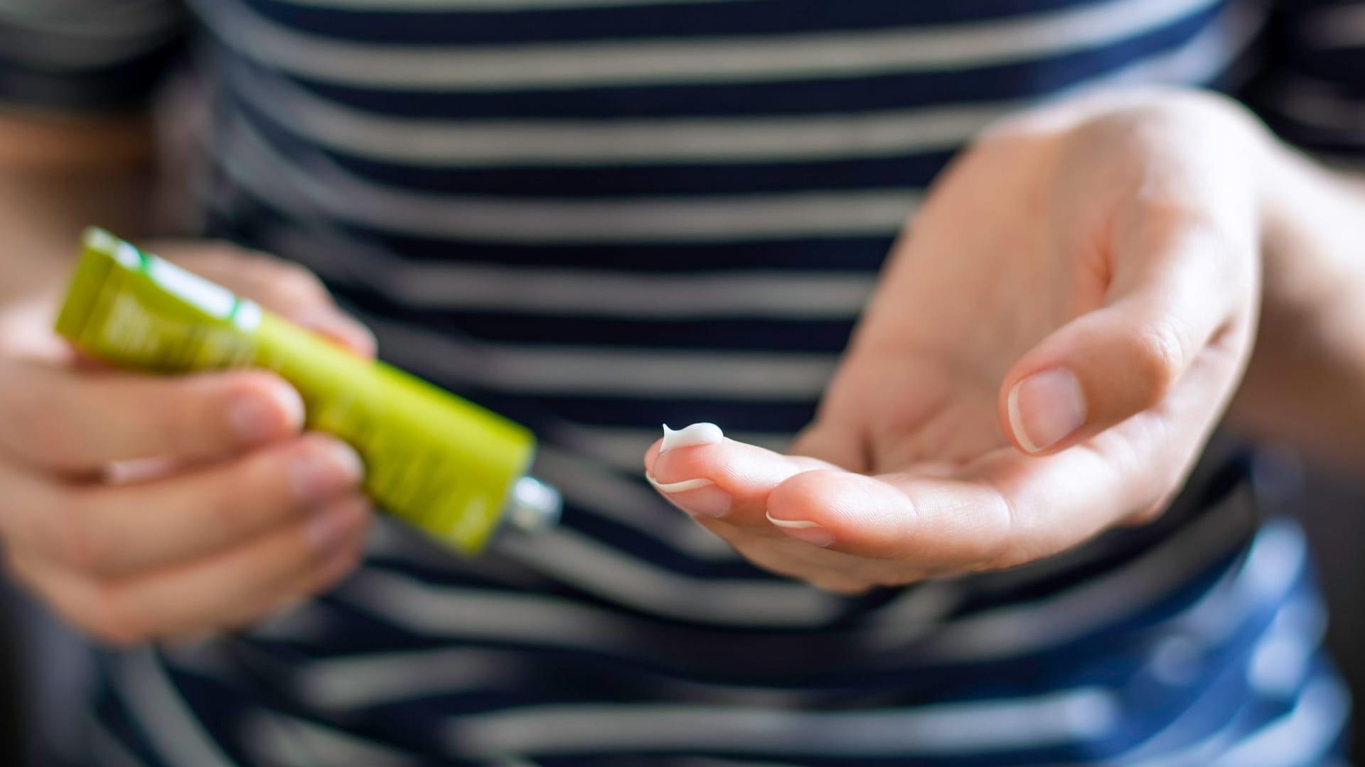 Frau mit Cremetube und etwas Creme auf dem Finger.