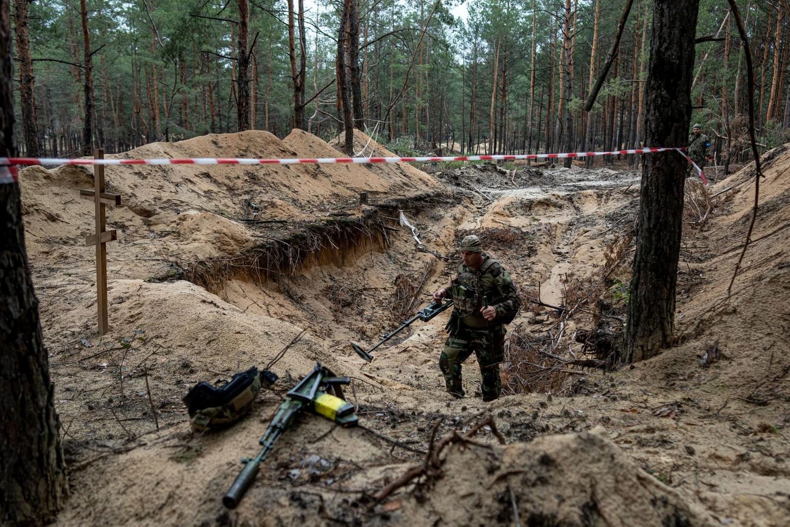 Ein Soldat untersucht eines der Gräber, die in einem Wald in Isjum gefunden wurden.