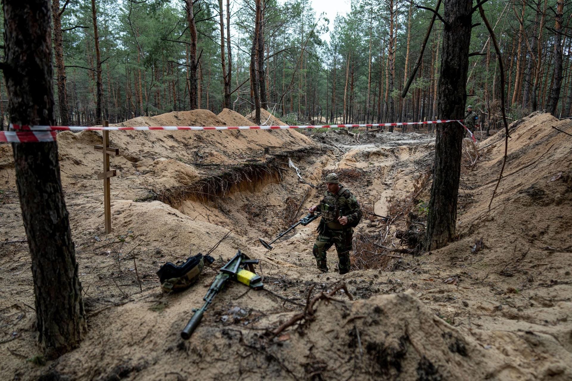 Ein Soldat untersucht eines der Gräber, die in einem Wald in Isjum gefunden wurden.