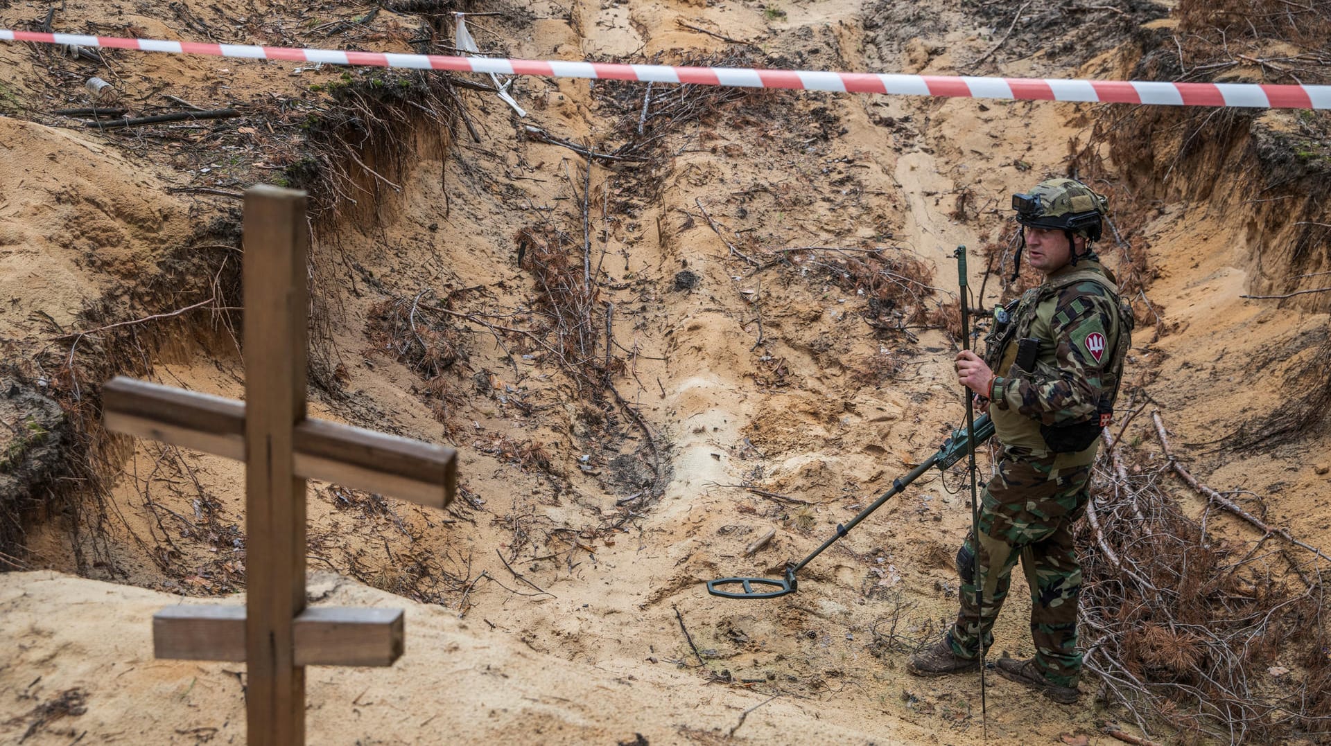 Ukrainian serviceman uses a metal detector to inspect a mass grave at a site on an improvised cemetery of civilians and Ukrainian soldiers in the town of Izium