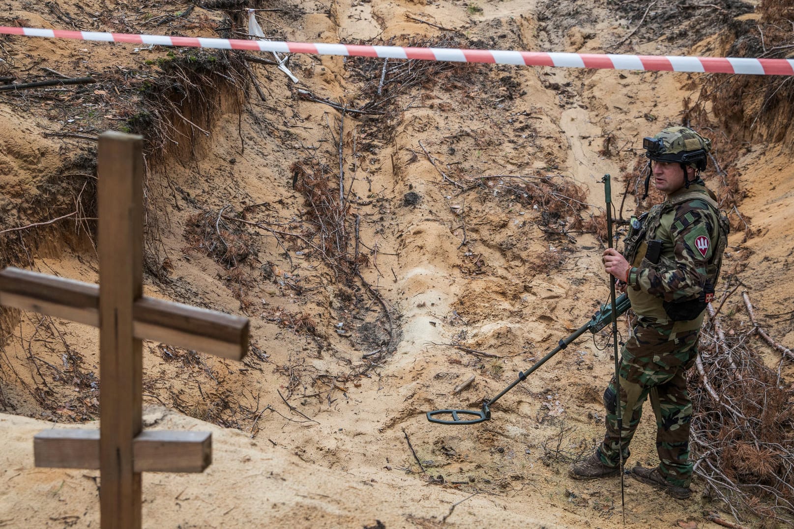 Ukrainian serviceman uses a metal detector to inspect a mass grave at a site on an improvised cemetery of civilians and Ukrainian soldiers in the town of Izium