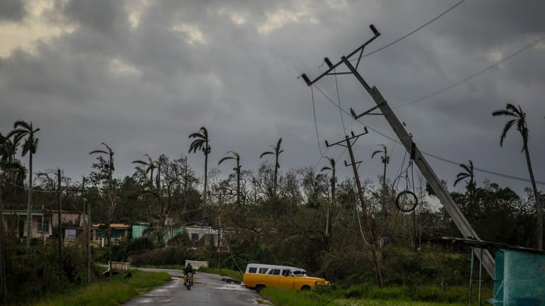 Ein amerikanischer Oldtimer fährt an vom Hurrikan "Ian" umgestürzten Strommasten vorbei.