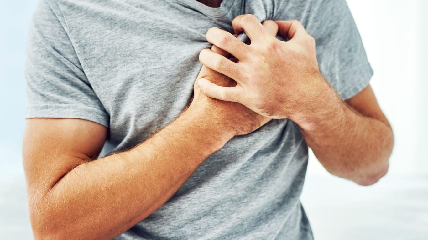Mann greift sich an die linke Brust. Ein Herzinfarkt in jüngeren Jahren deutet meist auf eine erbliche Vorbelastung hin.