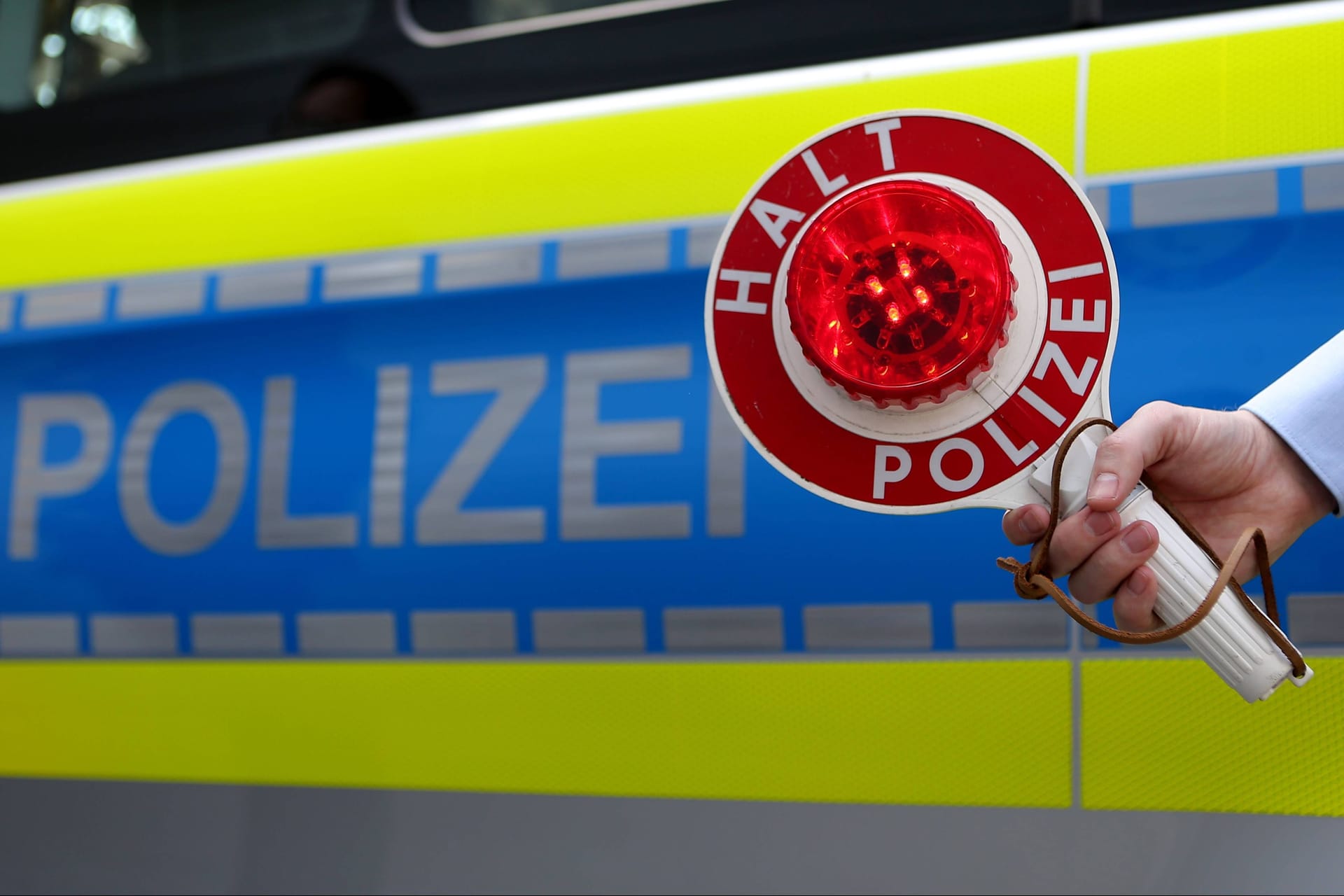 Ein Polizist hält eine Kelle mit der Anweisung, zu stoppen in der Hand (Symbolbild): Die Beamten hielten die beiden an, weil das Kennzeichenschild beschädigt war.