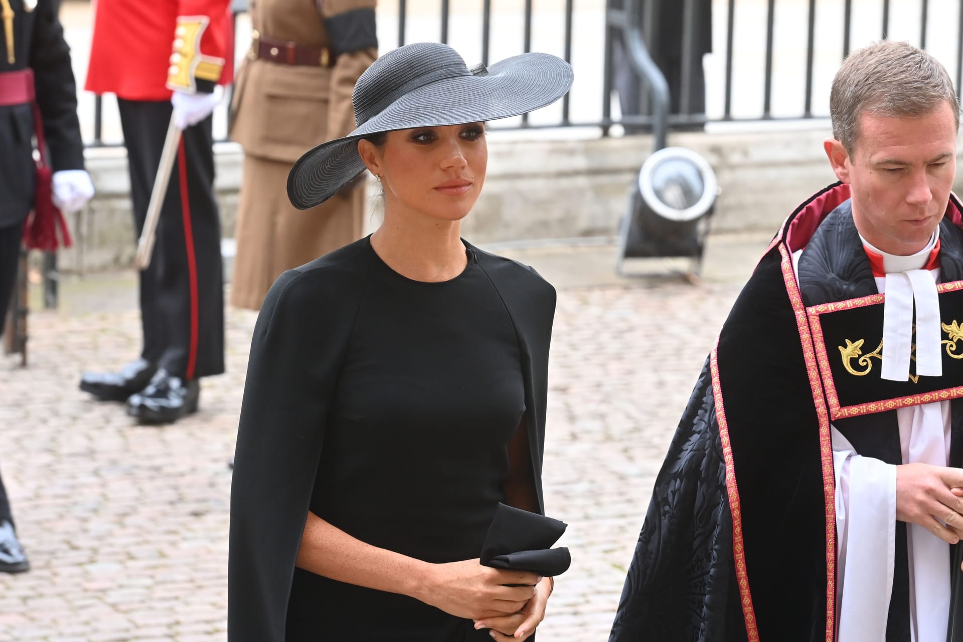 Herzogin Meghan nach dem Gottesdienst für die Queen: Die Frau von Prinz Harry trägt ein schlichtes schwarzes Kleid, darüber einen schwarzen Mantel und einen großen schwarzen Hut. Ihre Haare hat sie zu einem Knoten gebunden.