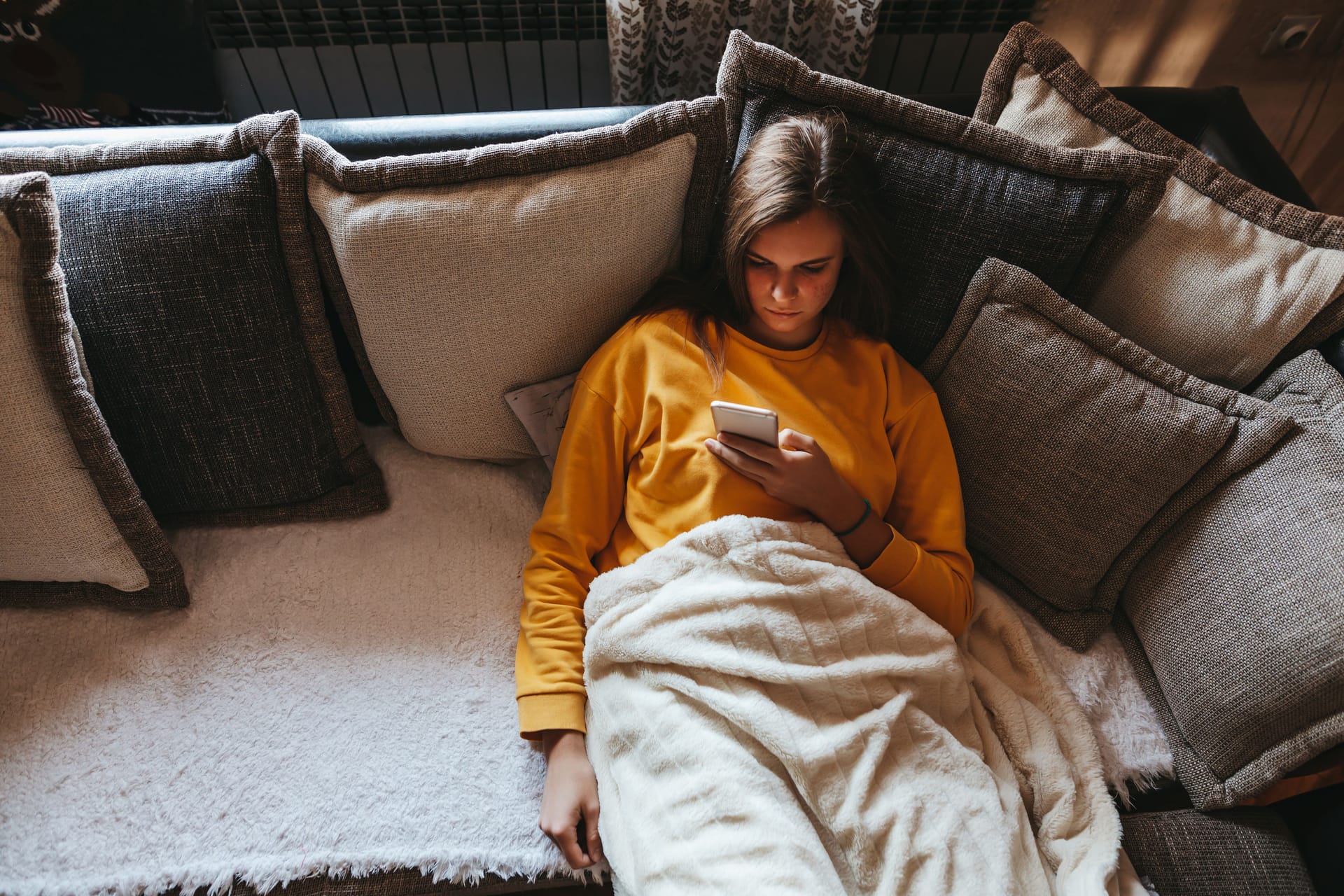 Eine Frau liegt auf dem Sofa und schaut auf ihr Handy.