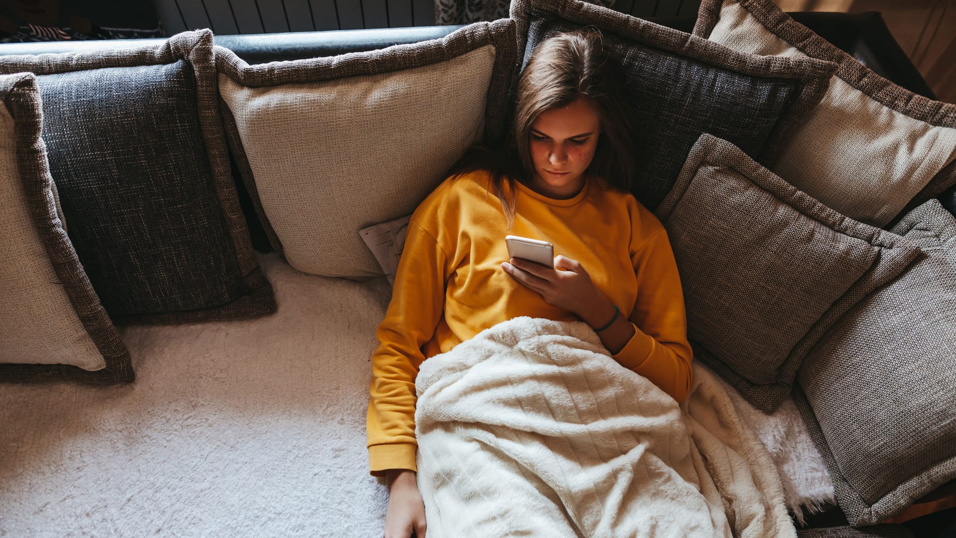 Eine Frau liegt auf dem Sofa und schaut auf ihr Handy.