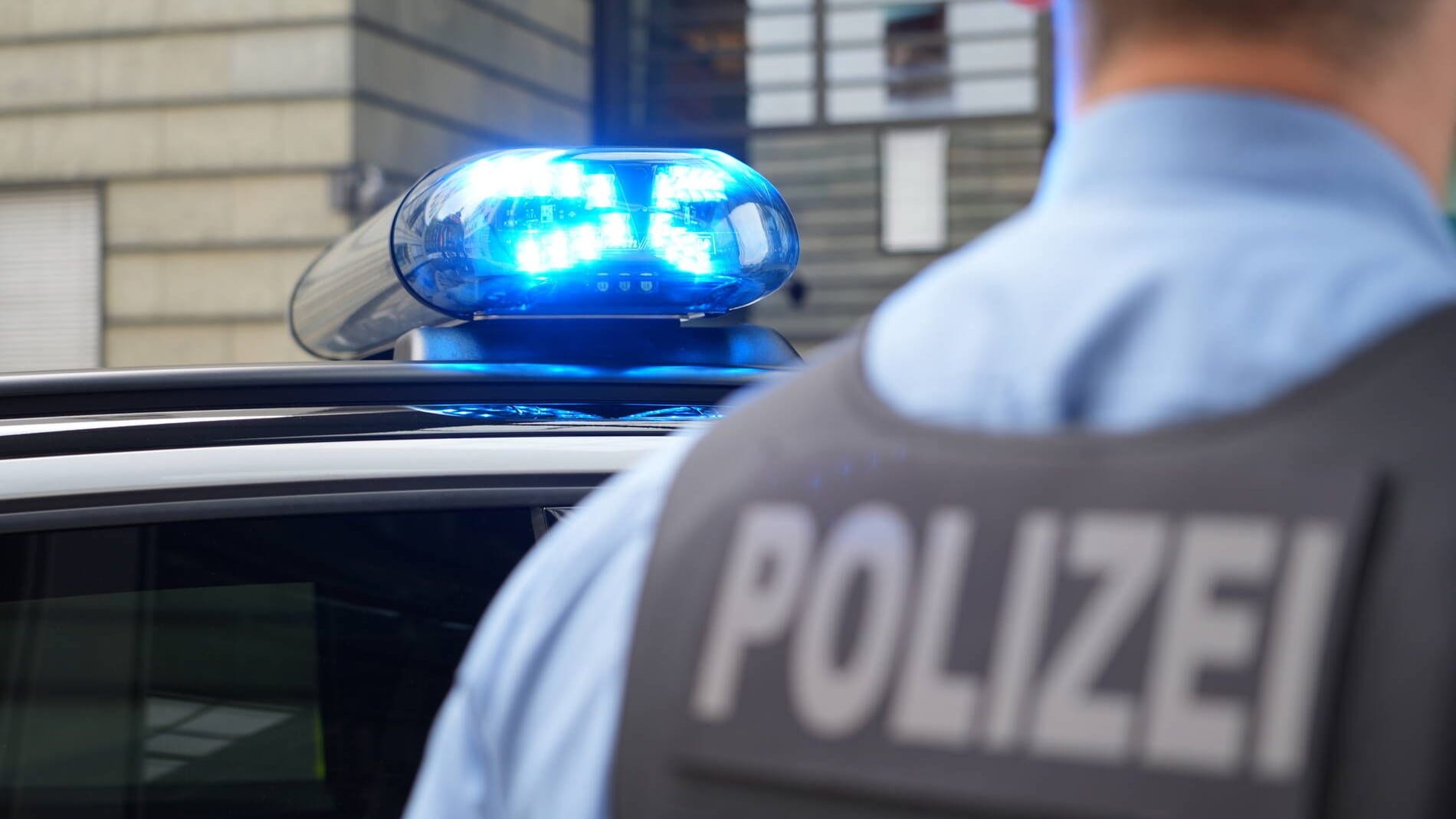 Polizei steht vor Polizeifahrzeug mit Blaulicht (Symbolbild): Die Polizei fahndet nach dem Täter.