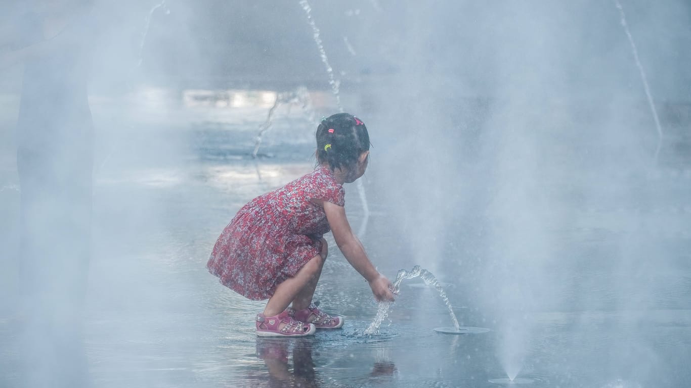 Ein kleines Mädchen spielt in einem Verdampfungskühler in Düsseldorf: Hohe Temperaturen sind besonders für Kleinkinder und ältere Menschen eine Gesundheitsgefahr.