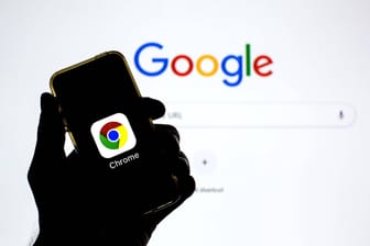Google-Suchleiste wird auf einem Bildschirm gezeigt und davor wird ein Handy mit dem Google-Chrome-Logo gezeigt.