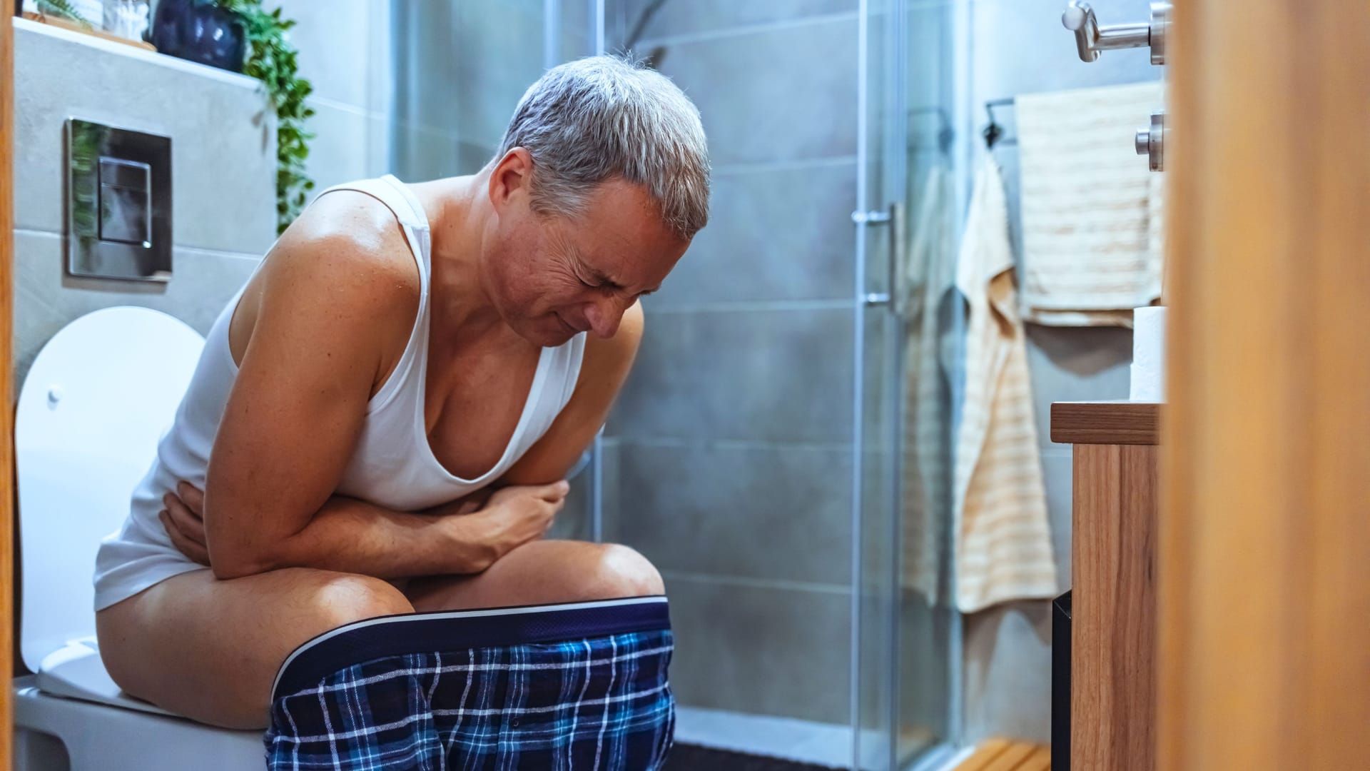 Ein Mann sitzt mit Schmerzen auf der Toilette.