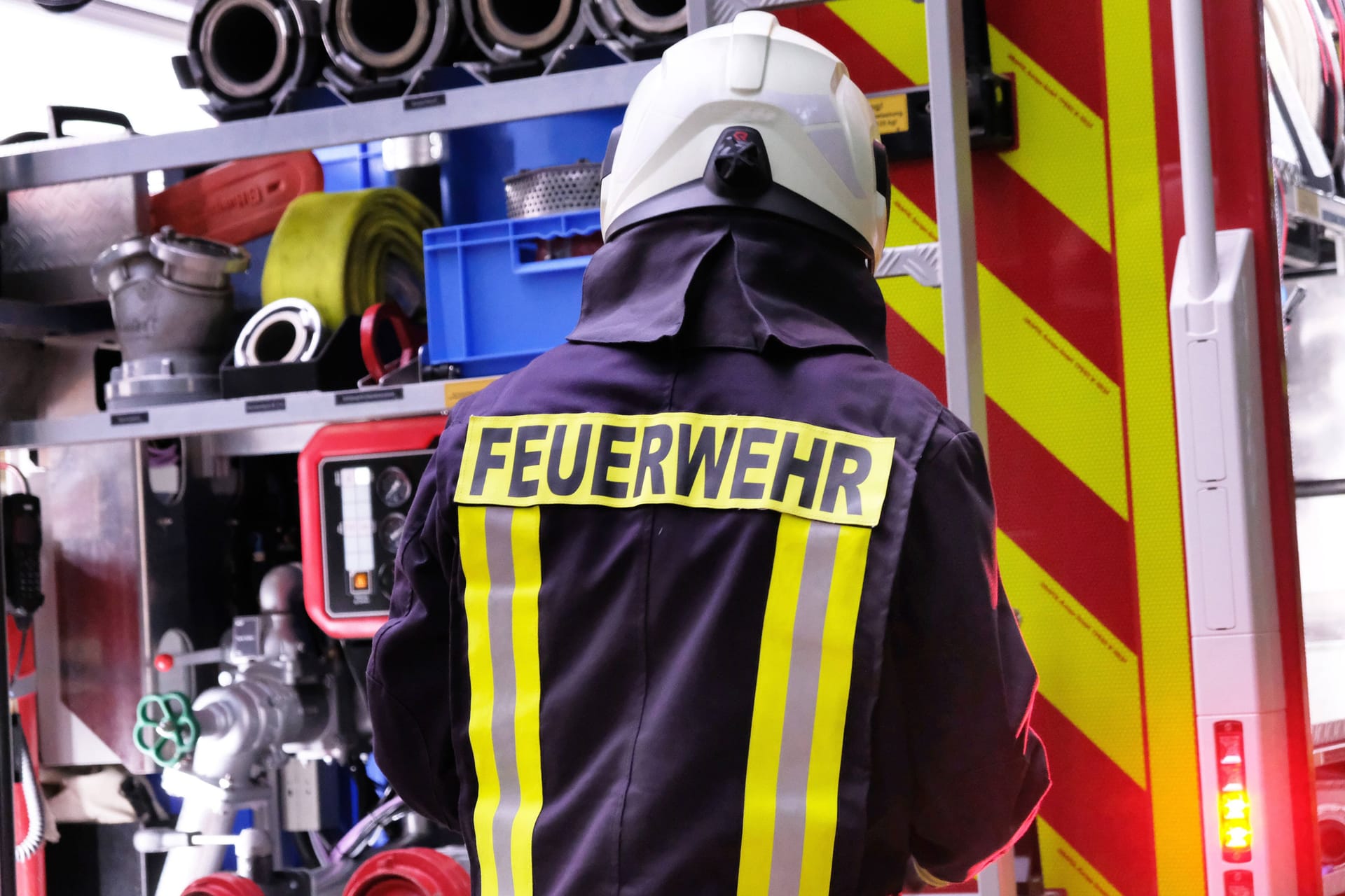 Ein Mitarbeiter der Feuerwehr steht vor einem Löschfahrzeug (Archivbild): Mehr als 20 Hausbewohner konnten sich ins Freie retten.