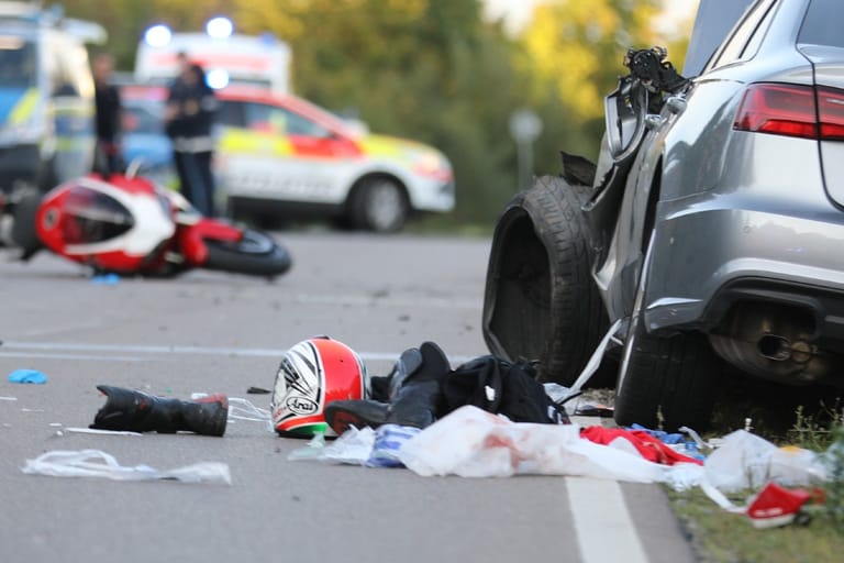 Die Unfallstelle: Die Front des Audis ist schwer beschädigt, auf der Straße liegen Sachen des Motorradfahrers.