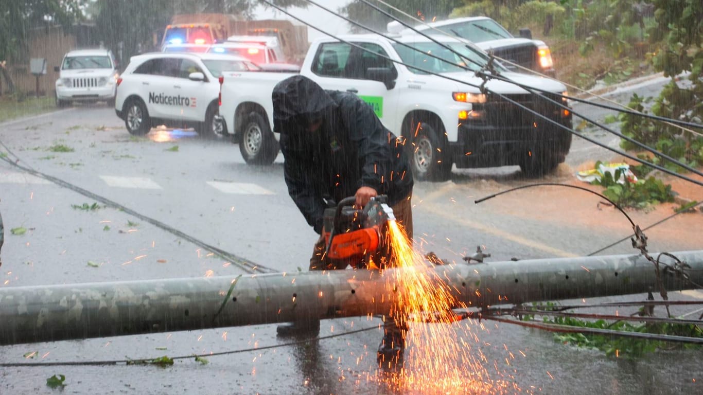 Puerto Rico, Cayey: Ein Arbeiter zerschneidet einen Strommasten, der durch den Hurrikan Fiona umgestürzt ist und eine Straße blockiert.