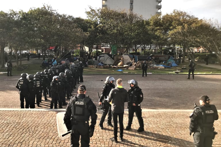Die Lage am Rathauspark in Westerland: Vorne in der Mitte ist Bürgermeister Nikolas Häckel zu sehen, der mit Polizisten darauf wartet, dass die Punks ihr Camp verlassen.