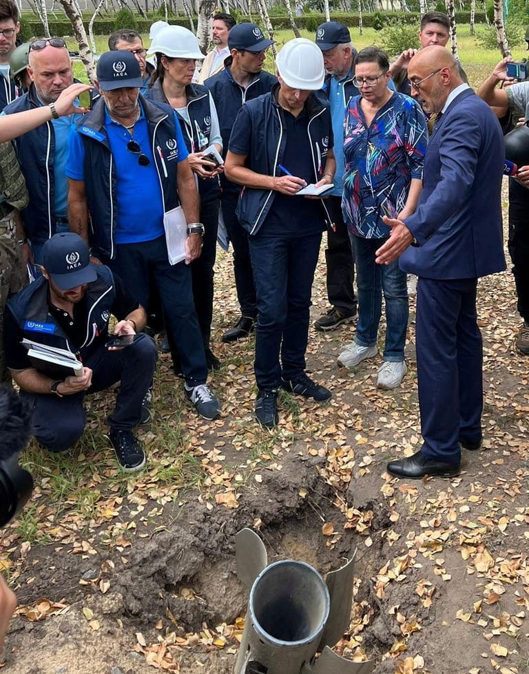 Grossi und seine Delegation vor einem Rakete-Überrest auf dem AKW-Gelände: Immer wieder treffen Einschläge die Anlage.