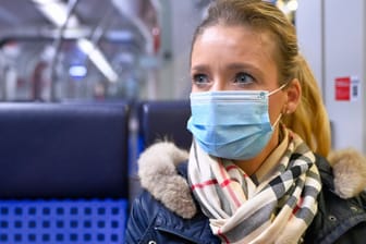 Eine Frau sitzt in einem Zug (Archivbild): Wer in Niedersachsen künftig im Nahverkehr mitfährt, braucht dort künftig nur noch eine OP-Maske zu tragen.