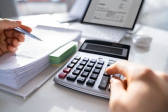 Ein Laptop, Unterlagen und ein Taschenrechner auf einem Tisch: Das Girokonto umzuziehen kann Kostenersparnisse bringen.