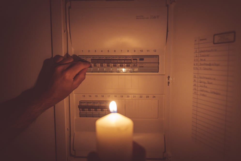 Eine Person steht mit einer Kerze vor einem Stromkasten (Symbolbild): Techniker arbeiten aktuell daran, dass die Störung behoben wird.