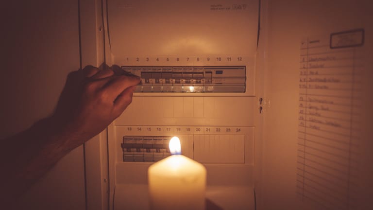 Eine Person steht mit einer Kerze vor einem Stromkasten (Symbolbild): Techniker arbeiten aktuell daran, dass die Störung behoben wird.