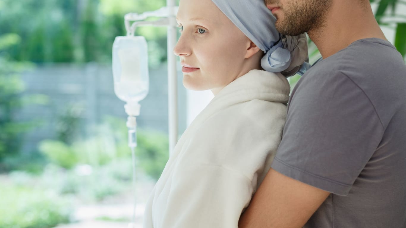 An Krebs erkrankte junge Frau wird von ihrem Mann umarmt