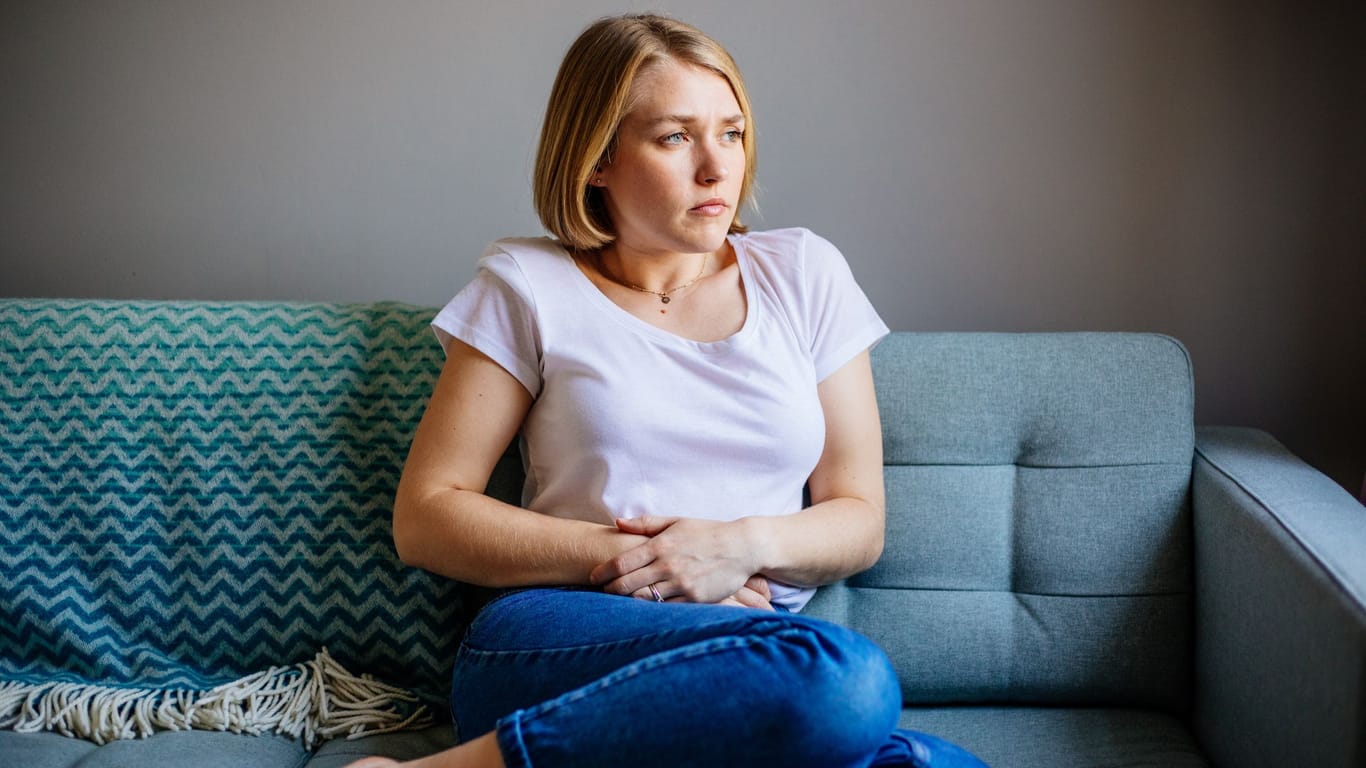 Nachdenklich wirkende Frau mit Bauchschmerzen auf dem Sofa