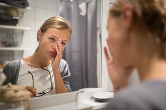 Eine Frau schaut müde in den Spiegel.