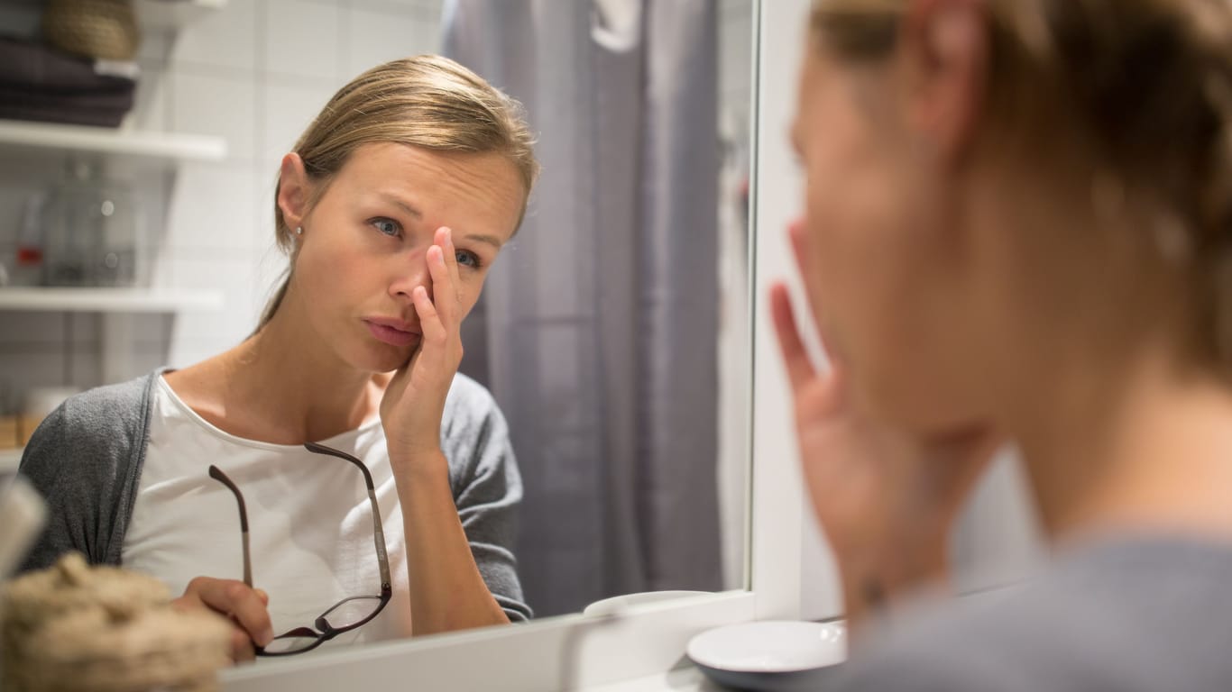 Eine Frau schaut müde in den Spiegel.