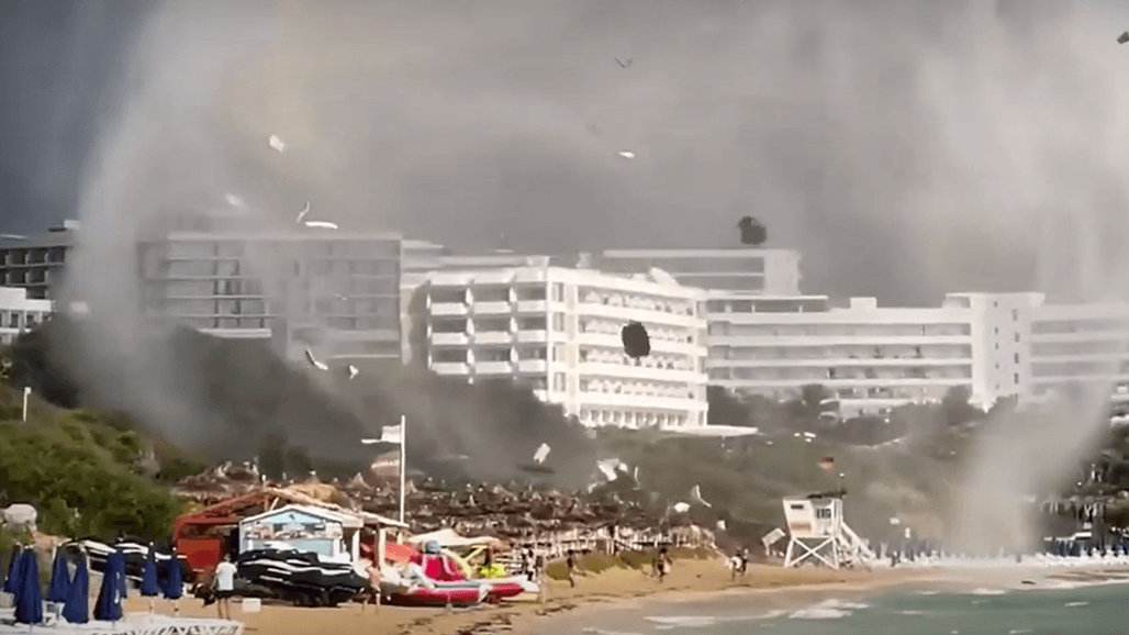 Eine Windhose fegt über einen Badestrand und wirbelt Schirme und Liegen in die Luft. Eine Windhose fegt über einen Badestrand und wirbelt Schirme und Liegen in die Luft.