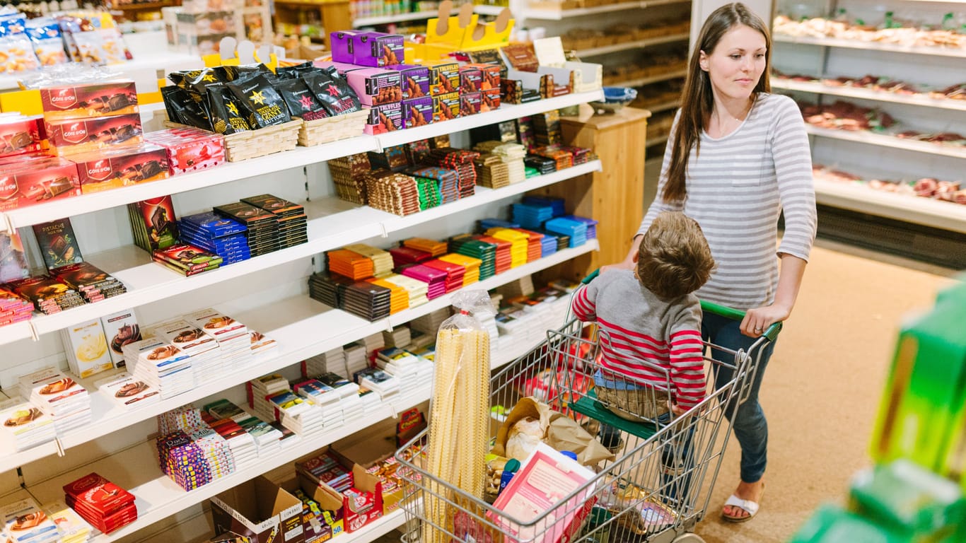 Eine Frau kauft mit Kind im Einkaufswagen ein. Das Regal mit den Süßwaren hat einige Lücken.