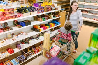 Eine Frau kauft mit Kind im Einkaufswagen ein. Das Regal mit den Süßwaren hat einige Lücken.