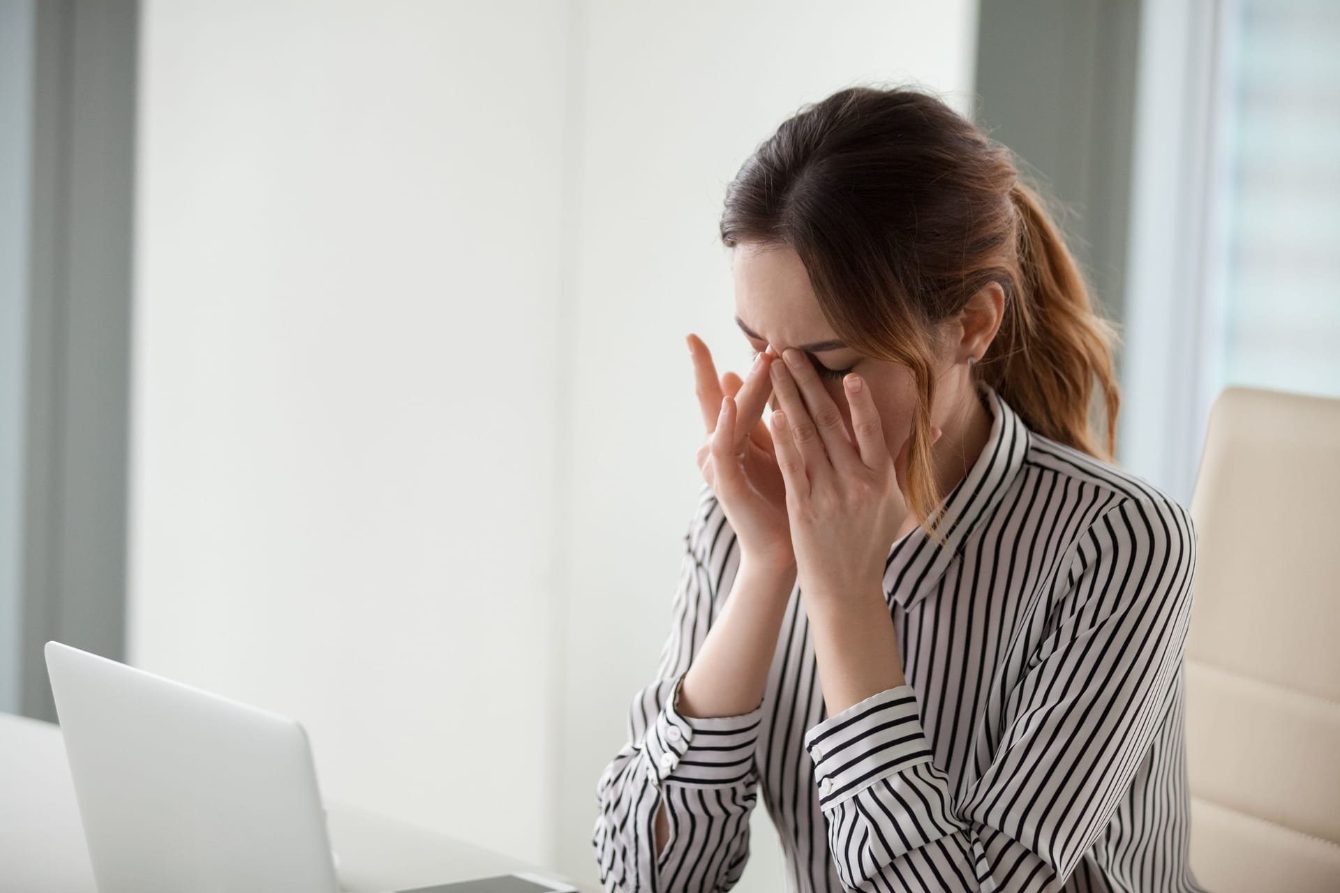 Eine Frau sitzt am Laptop und reibt sich die Augen.