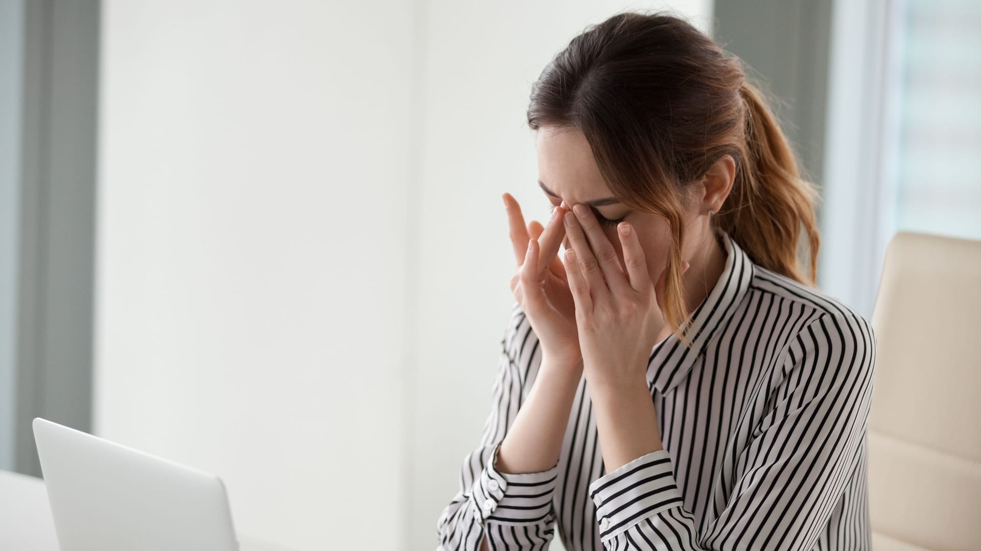 Eine Frau sitzt am Laptop und reibt sich die Augen.