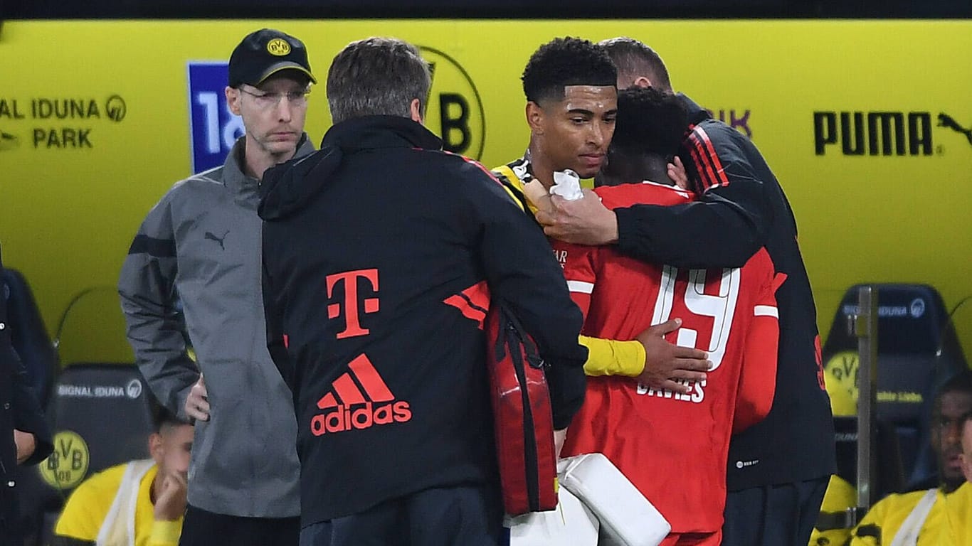Jude Bellingham und Alphonso Davies (r.): Der Kapitän von Borussia Dortmund entschuldigt sich noch auf dem Platz und nimmt seinen Gegenspieler, den er zuvor unbeabsichtigt mit dem Fuß im Gesicht getroffen hatte, in den Arm.
