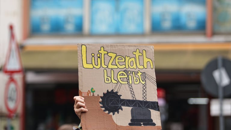 Eine Person hält ein Schild mit der Aufschrift "Lützerath bleibt" hoch.