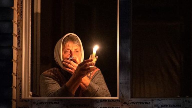 Eine Frau steht während eines Stromausfalls in der Ukraine mit einer Kerze in der Hand am Fenster.