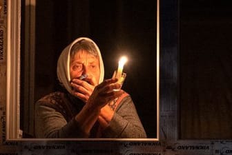 Eine Frau steht während eines Stromausfalls in der Ukraine mit einer Kerze in der Hand am Fenster.
