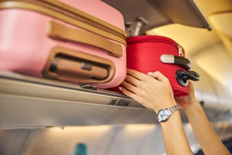 Eine Person verstaut Handgepäck im Flugzeug: Wer die großen Gepäckstücke vorreisen lässt, muss sich nur um sein Handgepäck kümmern.