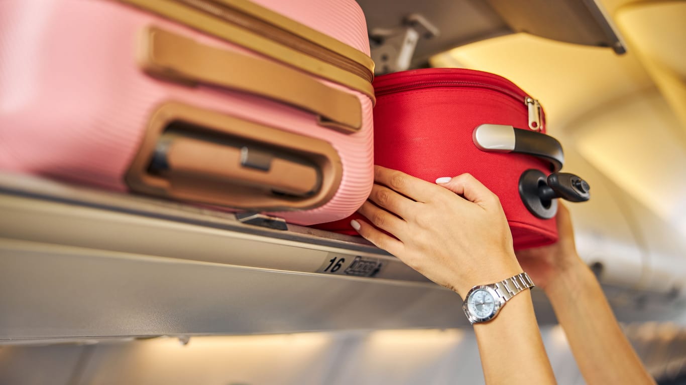 Eine Person verstaut Handgepäck im Flugzeug: Wer die großen Gepäckstücke vorreisen lässt, muss sich nur um sein Handgepäck kümmern.