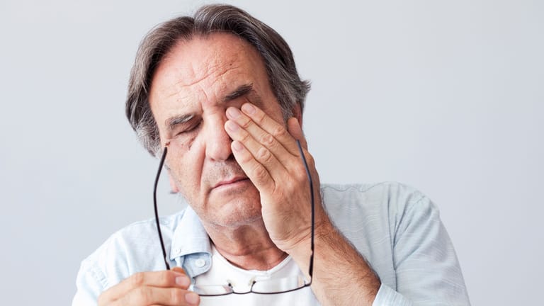 Müde wirkender älterer Mann reibt sich die Augen