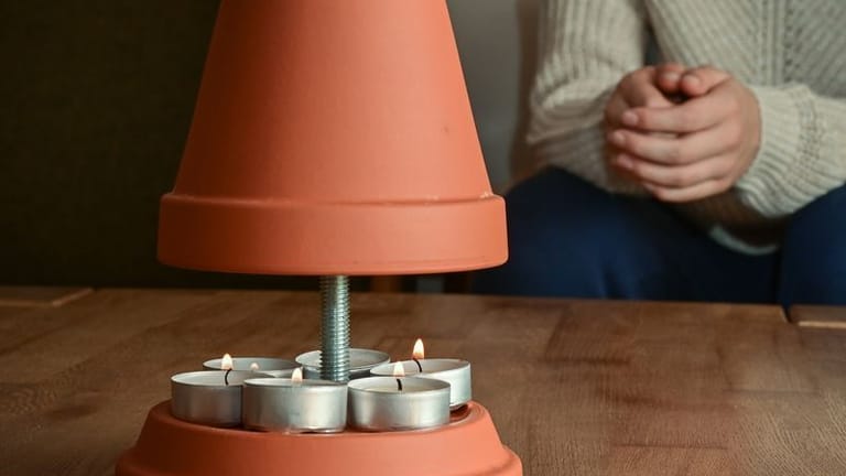 Eine Person wärmt sich an einem selbstgebauten Teelichtofen: Lassen Sie Kerzen nicht unbeaufsichtigt.
