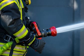 Ein Mitglied der Feuerwehr spritzt aus einem Schlauch mit Wasser (Symbolfoto): Die Ursache für das Feuer war zunächst unklar.