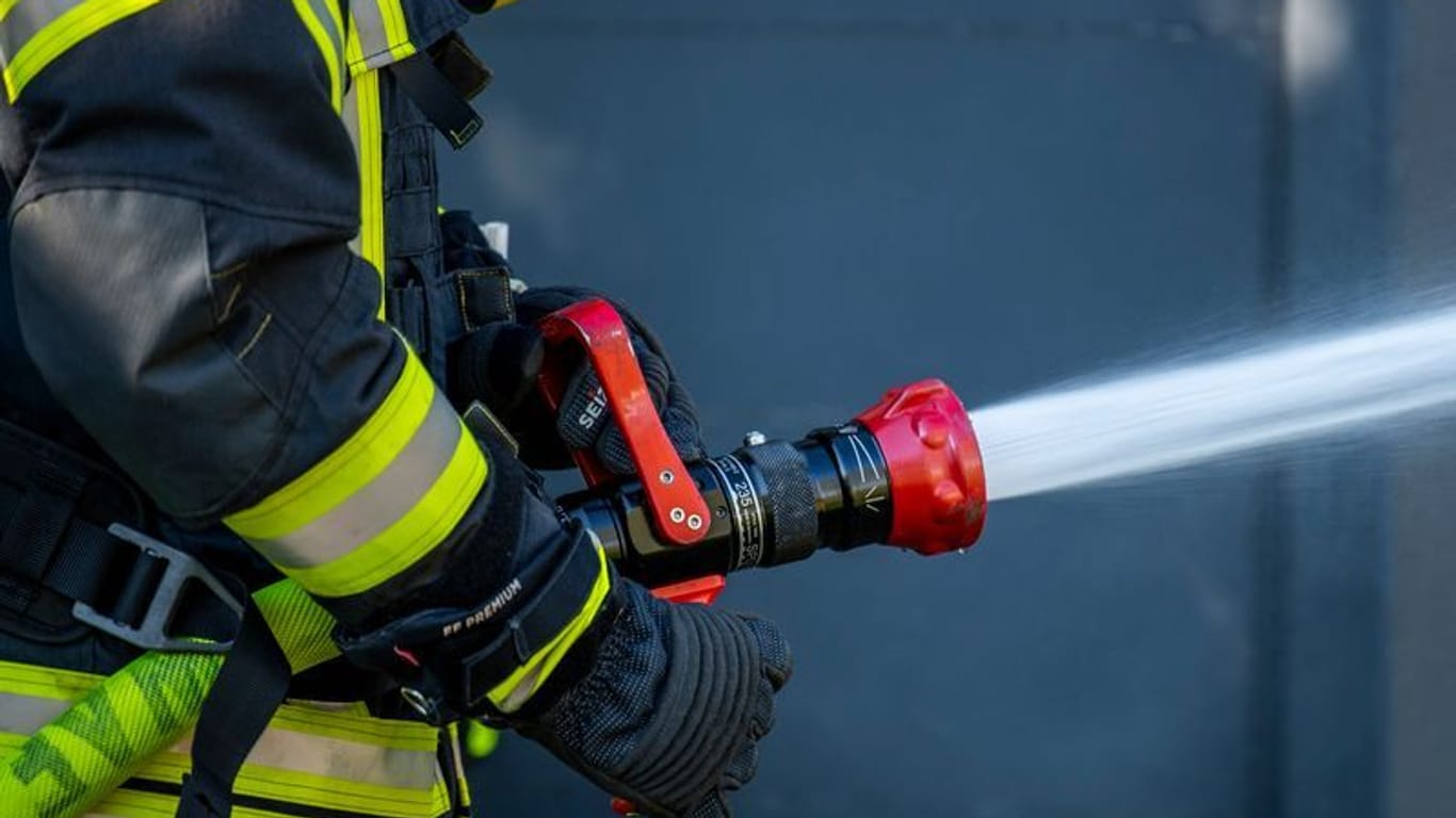 Ein Mitglied der Feuerwehr spritzt aus einem Schlauch mit Wasser (Symbolfoto): Die Ursache für das Feuer war zunächst unklar.