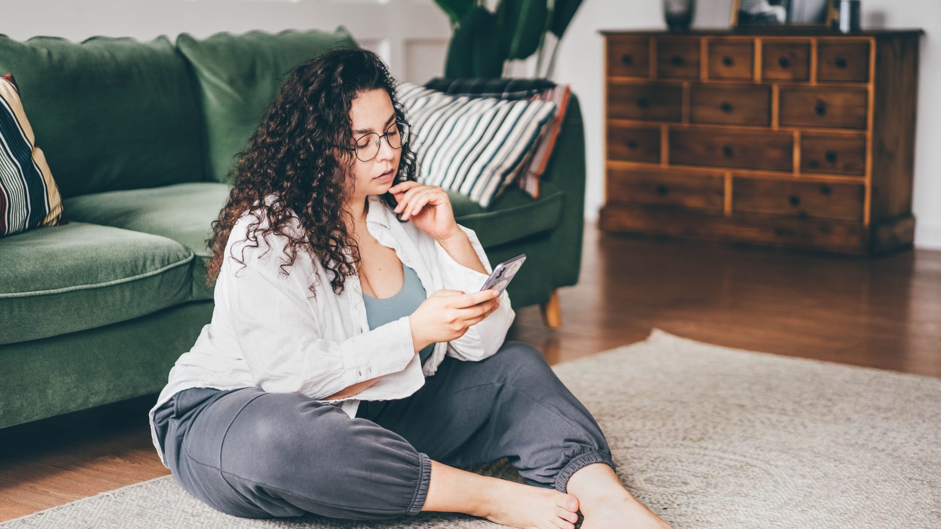 Eine Frau sitzt auf dem Boden und blickt auf ihr Smartphone.