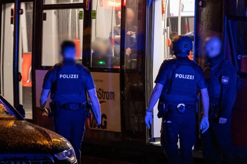 Polizisten stehen neben einer Straßenbahn in der Nähe des Tatorts.