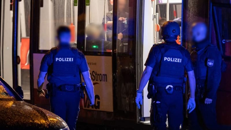 Polizisten stehen neben einer Straßenbahn in der Nähe des Tatorts.