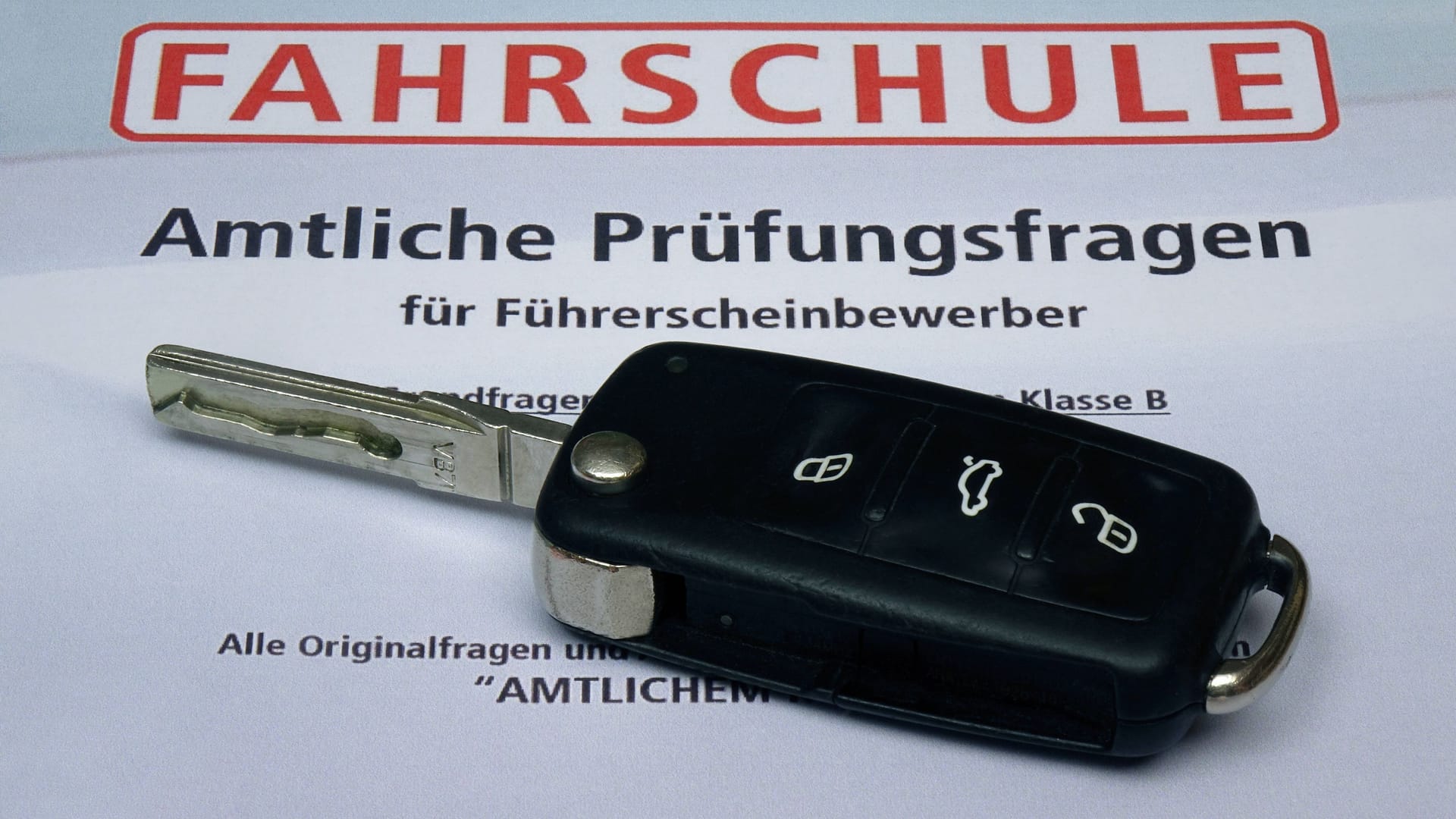 Auf den amtlichen Prüfungsfragen für die Fahrschule liegt ein Autoschlüssel.