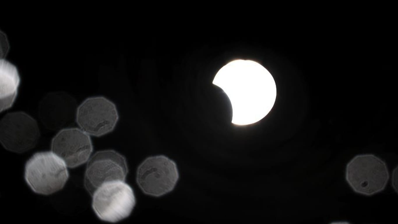 Die teilweise vom Mond verdeckte Sonne spiegelt sich während einer partiellen Sonnenfinsternis in einer im Sonnenschein glitzernden Regenpfütze