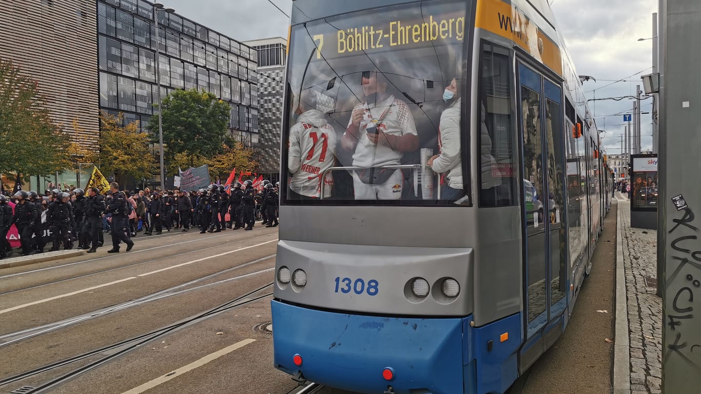 Eine Straßenbahn mit Fußballzuschauern auf dem Weg ins Stadion, dahinter eine Demo gegen steigende Preise. Am Samstag fand auch ein Bundesligaspiel in Leipzig statt.